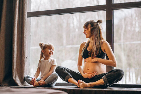 Tehotná žena cvičí jogu s jej dcérou