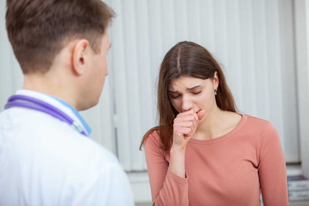 Young sick woman visiting doctor at the hospital. Female patient coughing while talking to her doctor