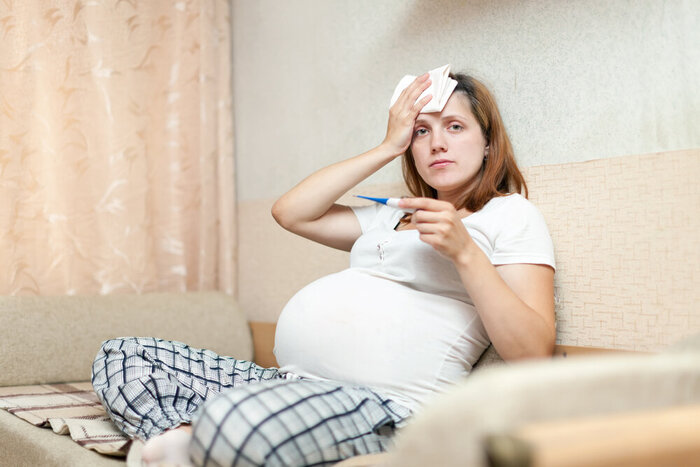pregnant woman sitting on sofa with thermometer in living room