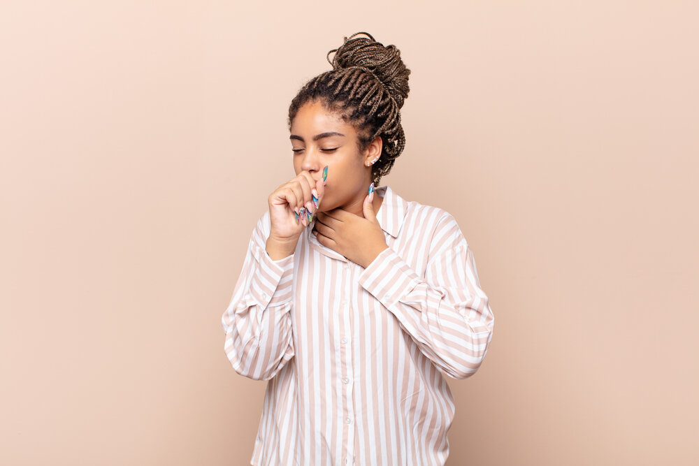 young afro woman feeling ill with a sore throat and flu symptoms, coughing with mouth covered