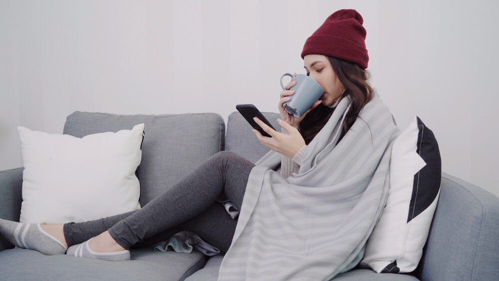 Beautiful attractive Asian woman using smartphone for texting and reading while lying on sofa when relax in living room at home. Lifestyle women at home in Christmas and New year holidays concept.