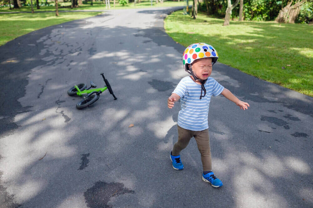 Cute upset stress sad unhappy little Asian 2 years old toddler baby boy child crying after fallen from his first bicycle / balance bike, Toddler's Terrible Twos and a child's tantrum in public concept