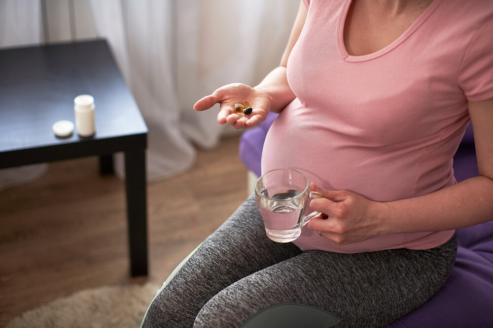 žena užíva vitamíny počas tehotenstva. tehotné dievča s pohárom vody a hrsťou vitamínov v ruke.