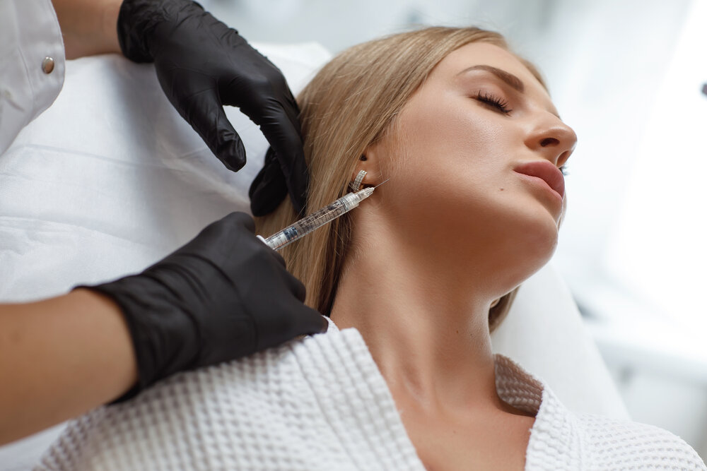 Kozmetička dáva injekciu s kyselinou hyalurónovou do ženskej tváre