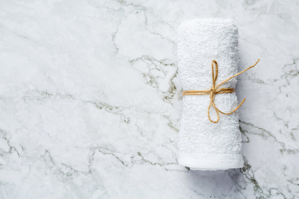 zrolovaný biely uterák na kúpeľné ošetrenie položený na podlahu z bieleho mramoru