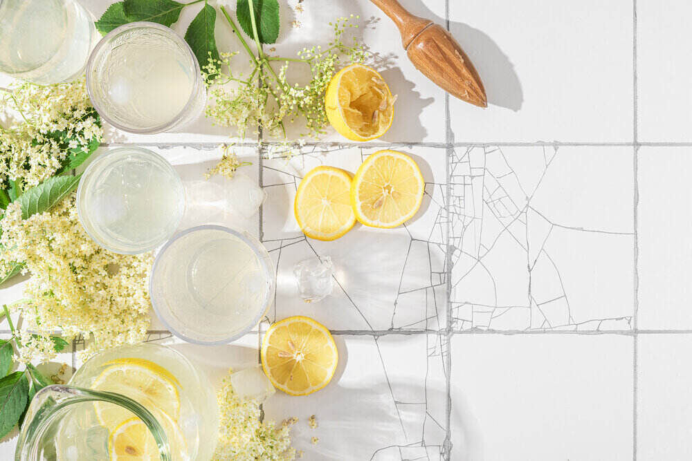 Čerstvá limonáda s citrónmi a bazovými kvetmi v pohároch na bielom stole 