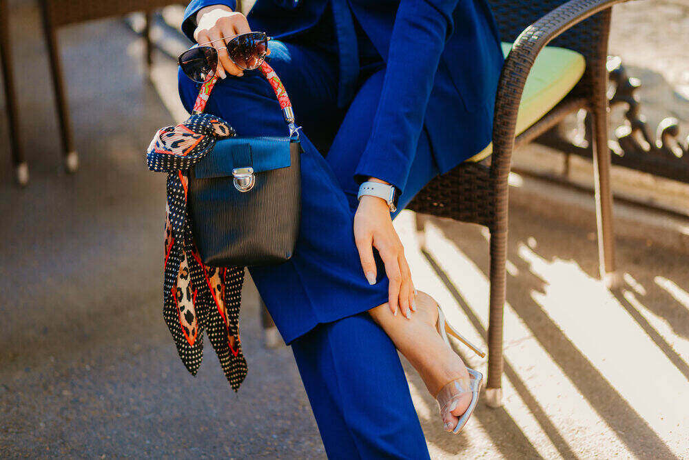 módne detaily a doplnky elegantnej ženy oblečenej v modrom obleku, držiacej štýlovú kabelku, slnečné okuliare a šál
