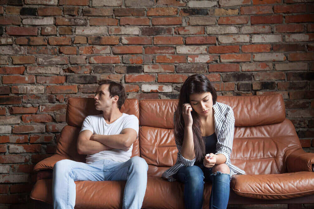 Frustrovaný pár sa po hádke nerozpráva, urazený tvrdohlavý žiarlivý muž sediaci ticho na pohovke so smutnou sklamanou ženou, problém so vzťahmi v manželstve