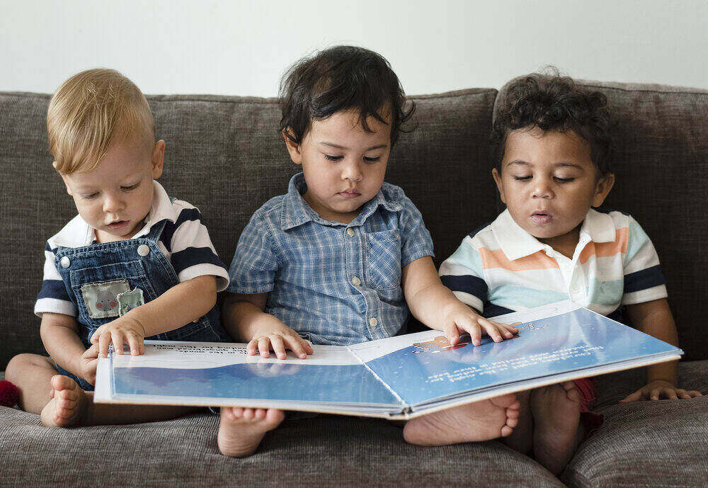 Traja malí chlapci čítajú knihu na pohovke