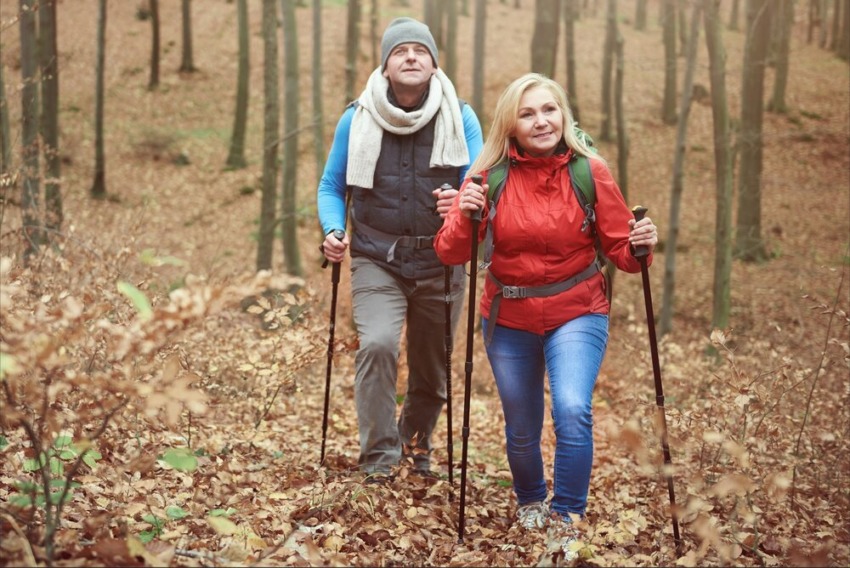 Starší pár sa prechádza lesom. V ruke drží trekingové palice.